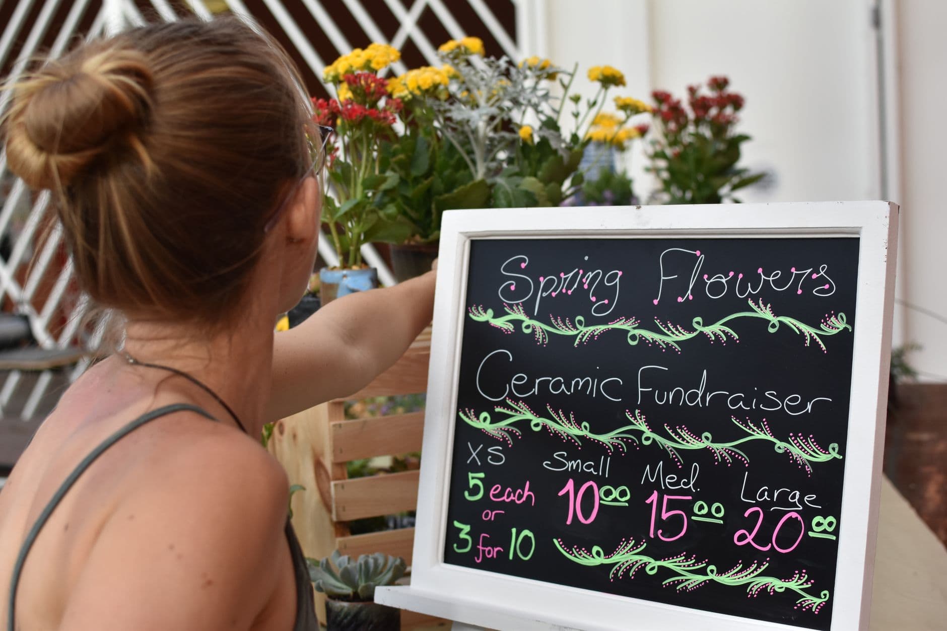 A woman arranging flowers at a ceramic fundraiser, featuring spring blooms and a pricing sign.